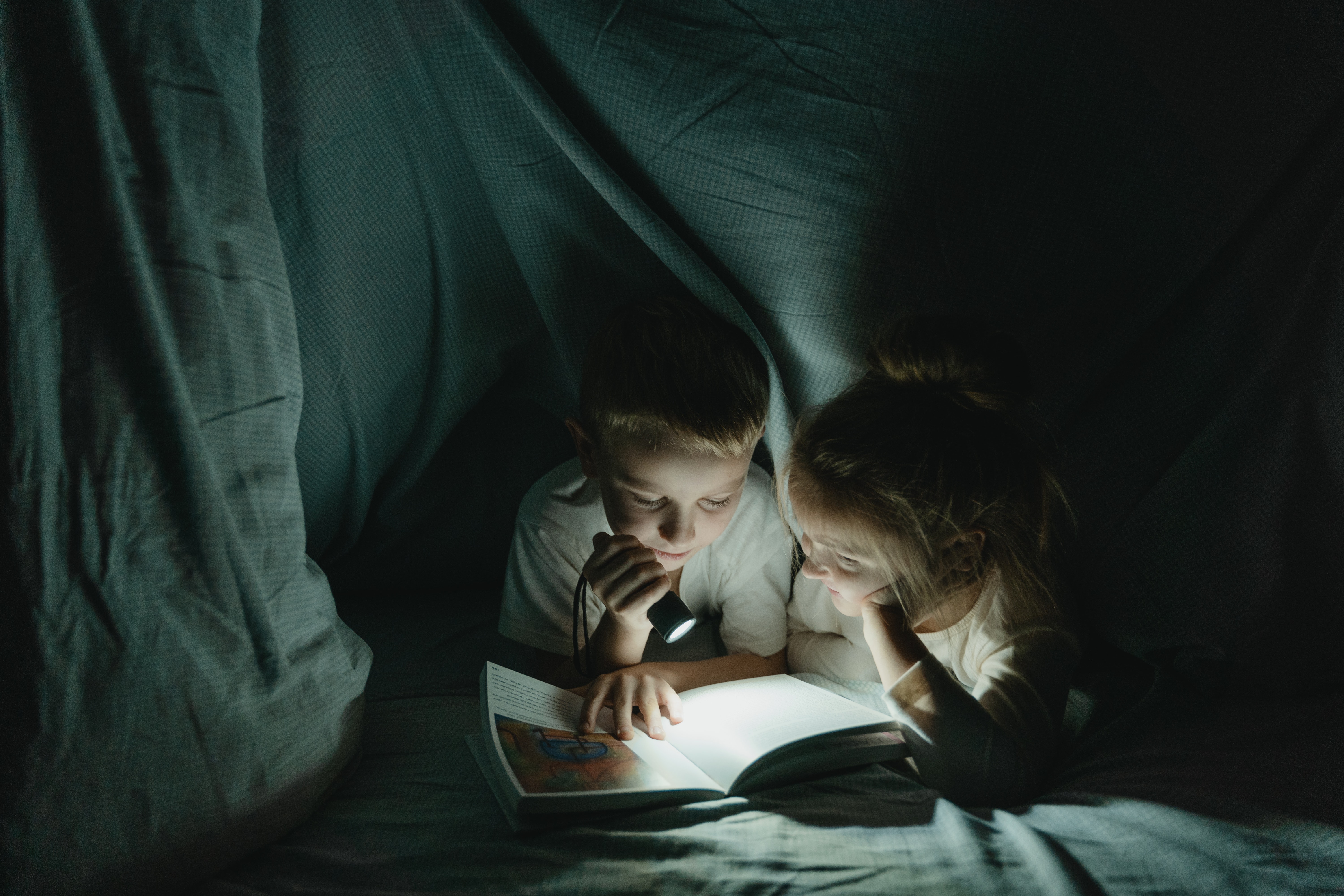 Kids reading by flashlight in a blanket fort
